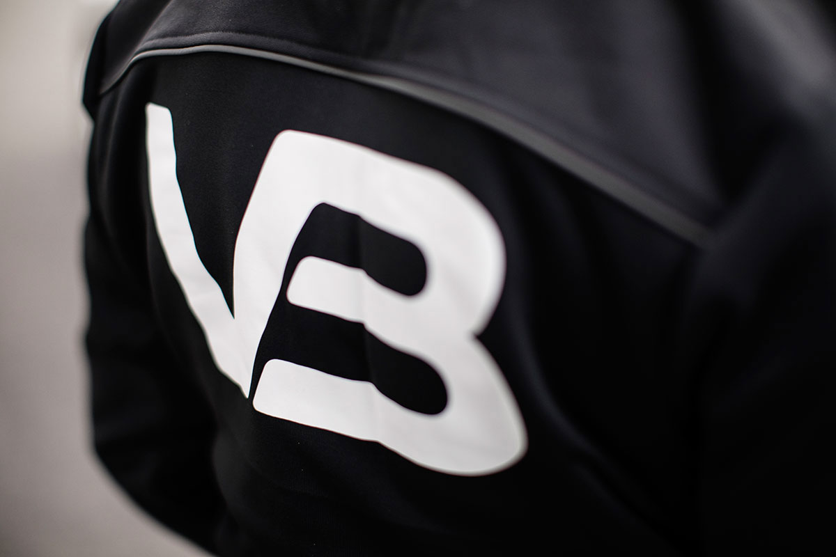Nærbilde av VB-logo på mørk rørlegger-arbeidsjakke.